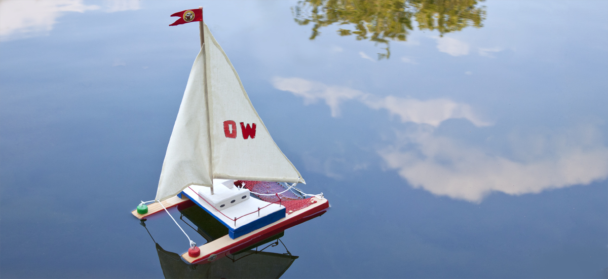 Model sailing ship on calm water with a red flag